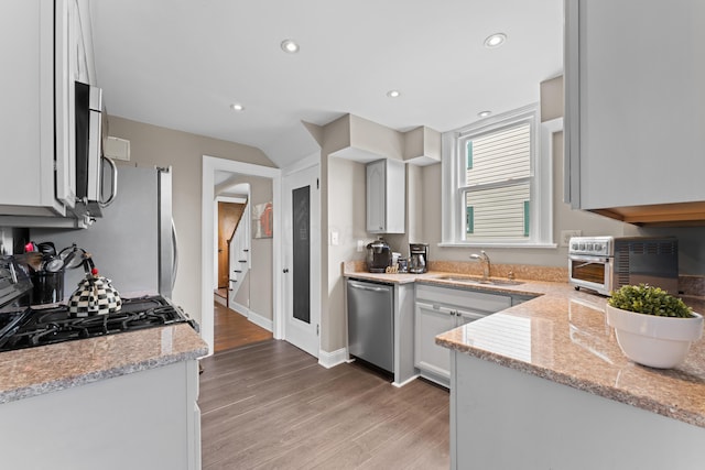 kitchen with stainless steel appliances, a sink, light wood finished floors, light stone counters, and recessed lighting