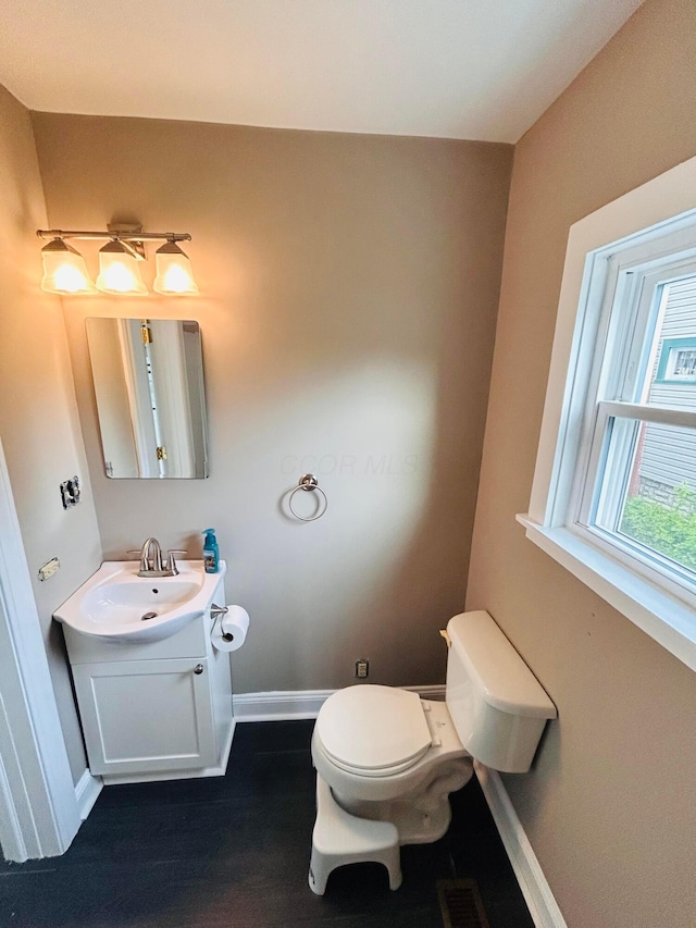 half bath with baseboards, vanity, toilet, and wood finished floors