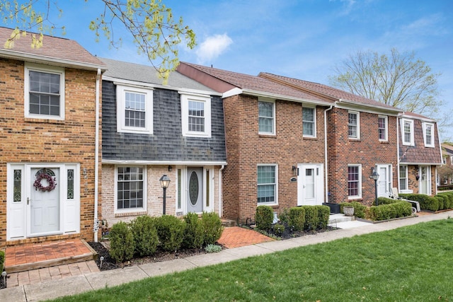 view of front of house with brick siding, a front yard, and a shingled roof