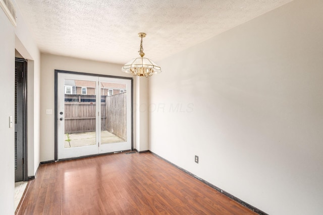 empty room with a notable chandelier, a textured ceiling, baseboards, and wood finished floors