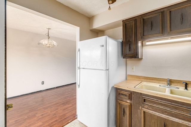 kitchen featuring light countertops, a sink, light wood-style floors, freestanding refrigerator, and dark brown cabinetry