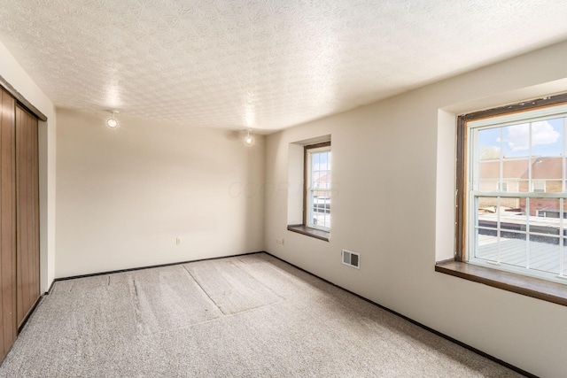 unfurnished bedroom featuring a closet, a textured ceiling, visible vents, and light colored carpet