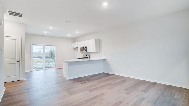 kitchen featuring white cabinets, visible vents, a peninsula, appliances with stainless steel finishes, and light wood-style floors