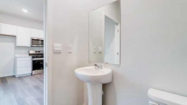 half bathroom featuring toilet, a sink, baseboards, and wood finished floors