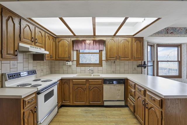 kitchen featuring a sink, a peninsula, dishwashing machine, under cabinet range hood, and white electric range oven