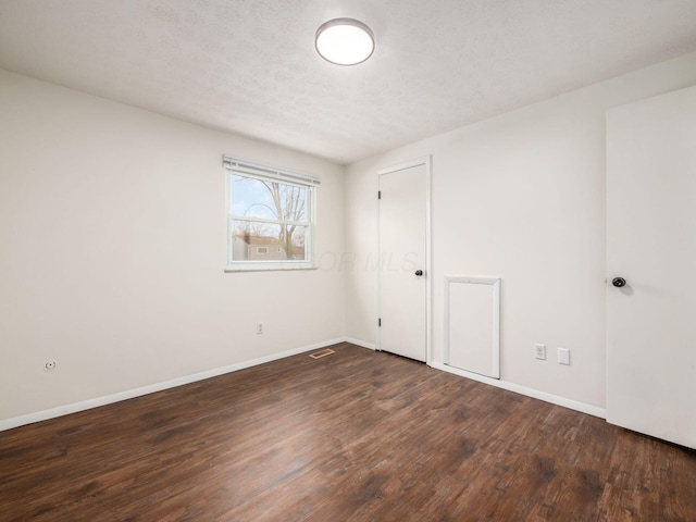 empty room with dark wood-type flooring, baseboards, and visible vents