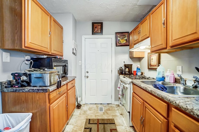 kitchen with a sink, gas range gas stove, a textured ceiling, under cabinet range hood, and brown cabinetry