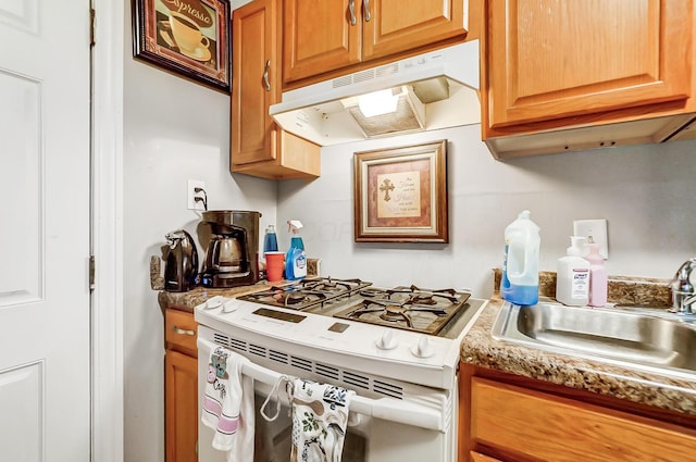 kitchen featuring white range with gas stovetop, under cabinet range hood, brown cabinetry, and a sink