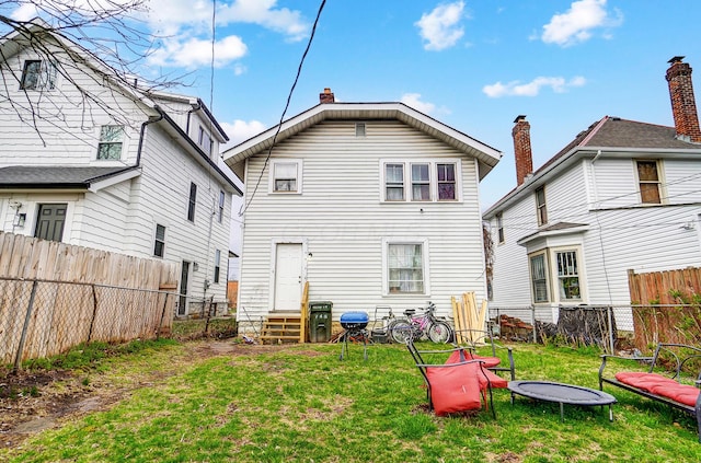 rear view of property with entry steps, a fenced backyard, and a lawn