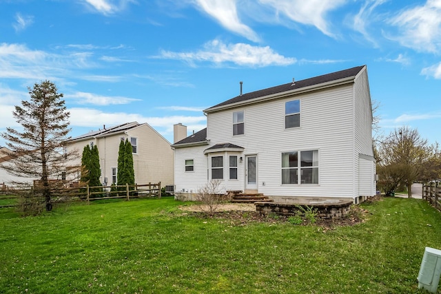 rear view of house with entry steps, fence, and a lawn