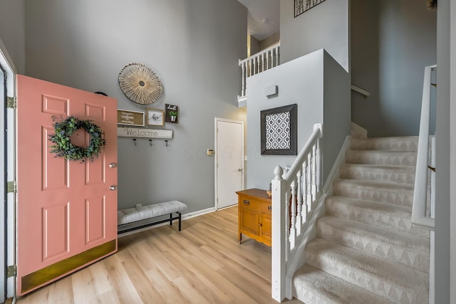 foyer entrance featuring baseboards, a towering ceiling, wood finished floors, and stairs