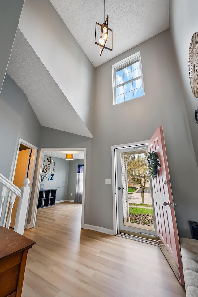 entryway with a notable chandelier, baseboards, light wood-style flooring, a textured ceiling, and high vaulted ceiling