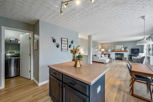 kitchen with light wood-style flooring, a center island, a textured ceiling, a fireplace, and pendant lighting