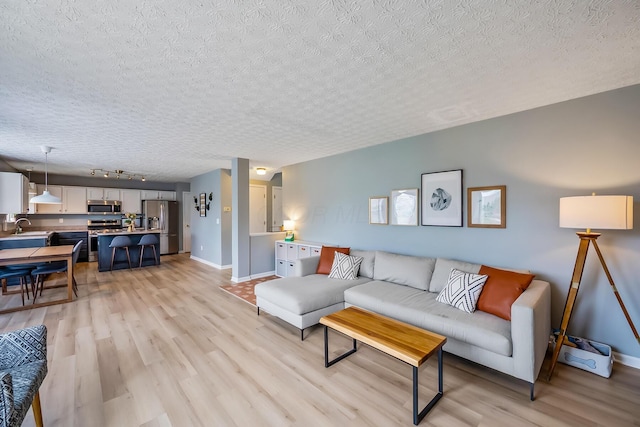 living room featuring baseboards, light wood-type flooring, a textured ceiling, and track lighting