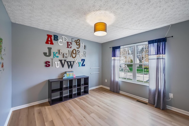 empty room with visible vents, light wood-style flooring, baseboards, and a textured ceiling