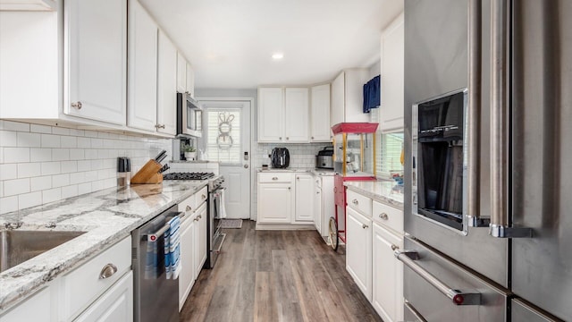 kitchen with white cabinetry, decorative backsplash, dark wood finished floors, light stone counters, and appliances with stainless steel finishes