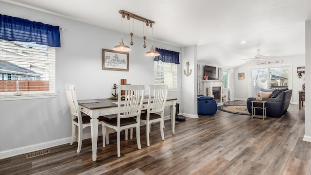 dining space with visible vents, a fireplace, ceiling fan, wood finished floors, and lofted ceiling