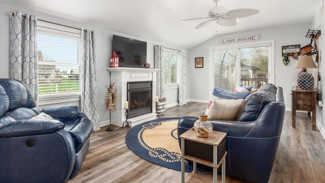 living room with baseboards, wood finished floors, a ceiling fan, lofted ceiling, and a glass covered fireplace