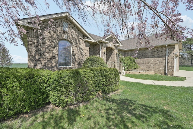 view of front of property with a shingled roof, brick siding, and a front lawn