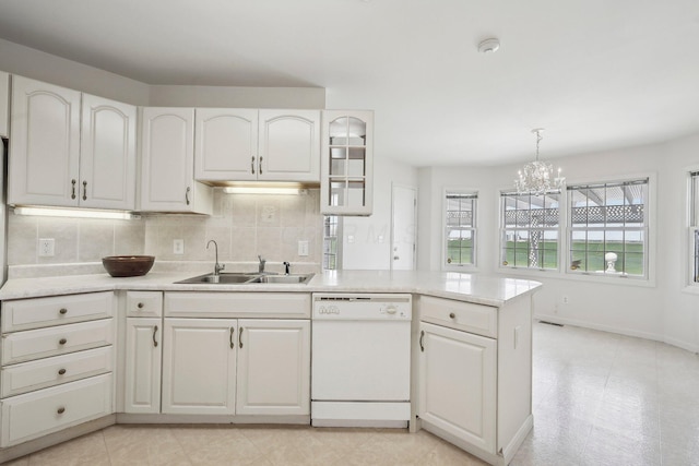 kitchen featuring dishwasher, a sink, light countertops, a chandelier, and backsplash