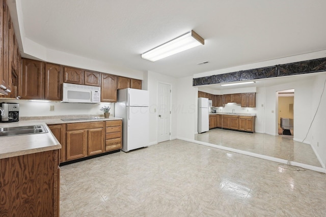 kitchen with a sink, light countertops, white appliances, and baseboards