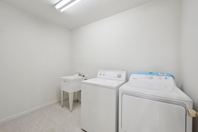 clothes washing area featuring washing machine and clothes dryer, light floors, laundry area, and baseboards