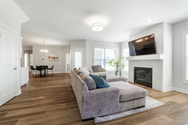 living area with a notable chandelier, a glass covered fireplace, wood finished floors, and baseboards