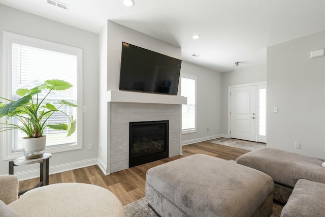 living room with light wood-style flooring, visible vents, recessed lighting, a brick fireplace, and baseboards