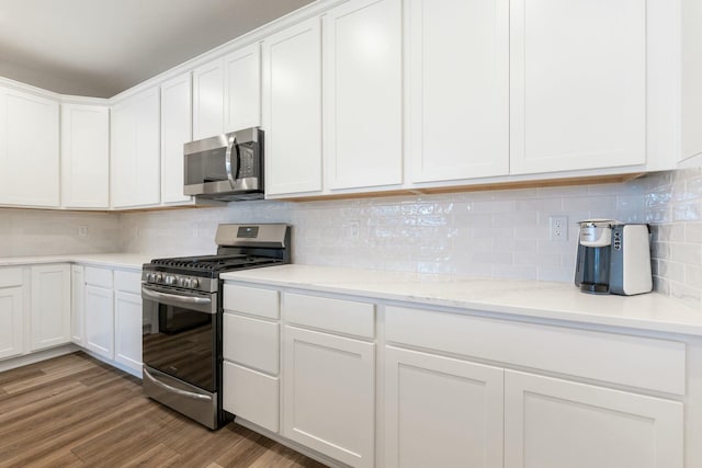 kitchen featuring white cabinets, appliances with stainless steel finishes, light stone counters, light wood finished floors, and backsplash