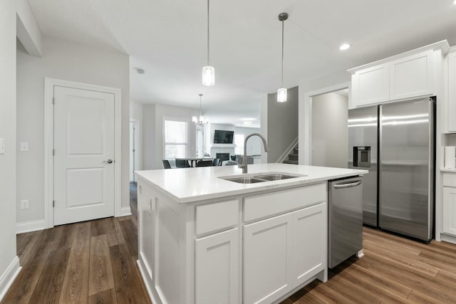 kitchen with dark wood-type flooring, a kitchen island with sink, a sink, and appliances with stainless steel finishes
