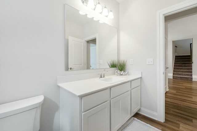 half bathroom featuring toilet, vanity, wood finished floors, and baseboards