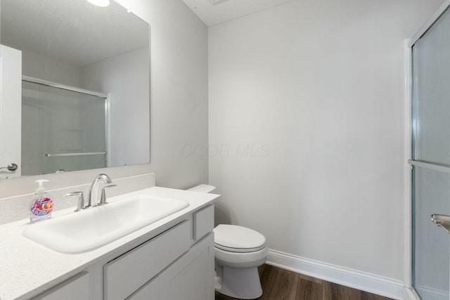 full bath featuring a shower with door, vanity, baseboards, toilet, and wood finished floors