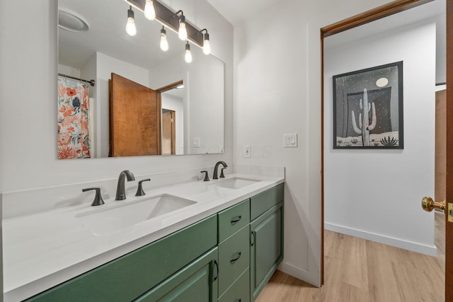 full bath featuring double vanity, baseboards, a sink, and wood finished floors