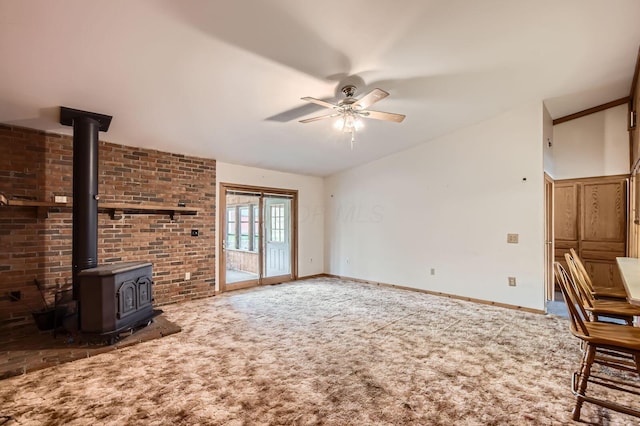 unfurnished living room featuring a wood stove, ceiling fan, carpet flooring, and baseboards