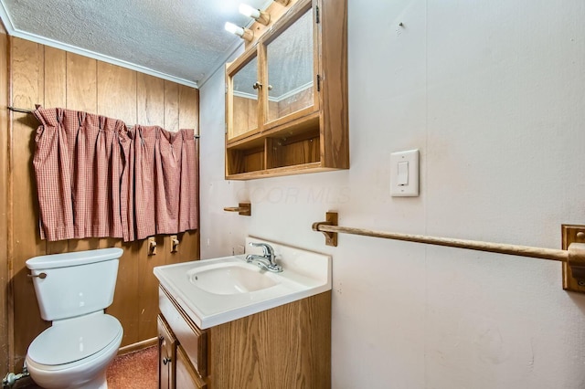 half bath featuring wooden walls, toilet, vanity, and a textured ceiling