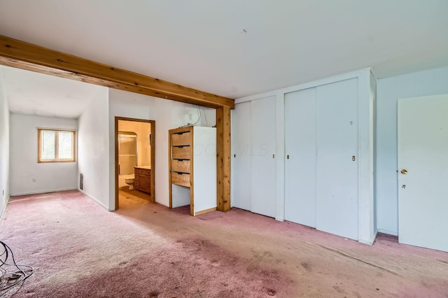 unfurnished bedroom with multiple closets, ensuite bath, and light carpet