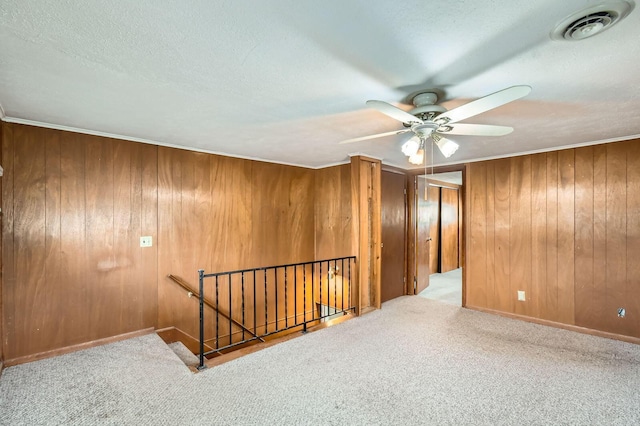 interior space featuring wooden walls, a textured ceiling, carpet floors, visible vents, and ceiling fan
