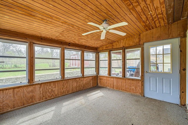 unfurnished sunroom with wood walls, plenty of natural light, vaulted ceiling, and a ceiling fan