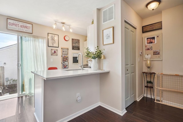 interior space featuring dark wood-type flooring, a peninsula, visible vents, a sink, and baseboards