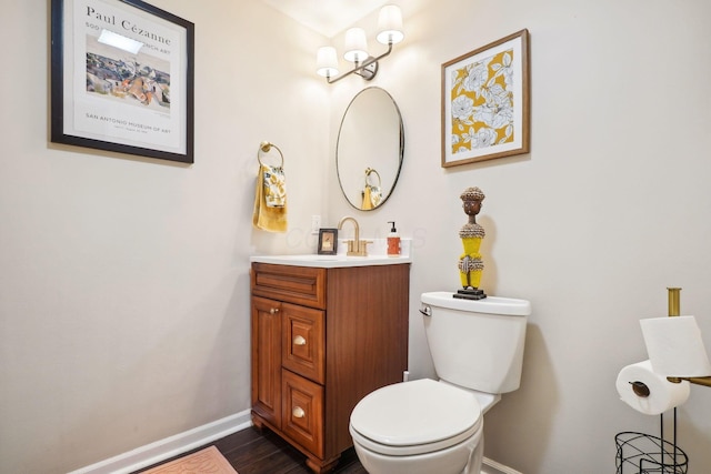 half bath with vanity, baseboards, toilet, and wood finished floors