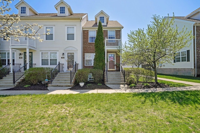 view of property with brick siding, a balcony, and a front lawn