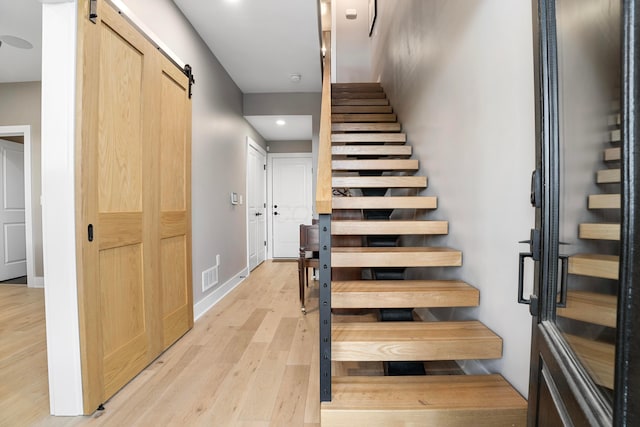 staircase featuring a barn door, recessed lighting, wood finished floors, visible vents, and baseboards