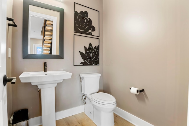 half bath with baseboards, wood finished floors, and toilet