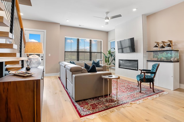 living room featuring baseboards, a fireplace, light wood-style floors, and ceiling fan