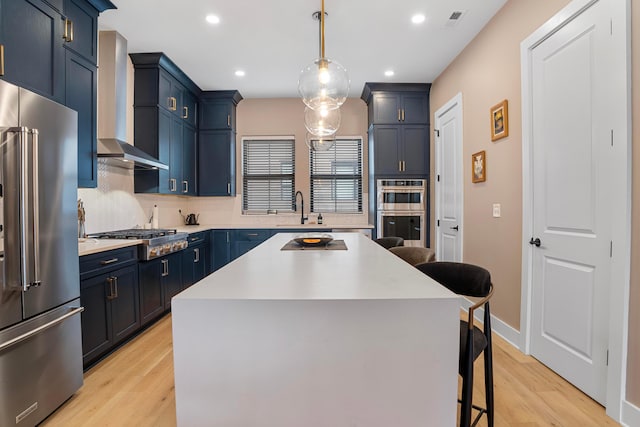 kitchen featuring a breakfast bar, wall chimney range hood, appliances with stainless steel finishes, and blue cabinets