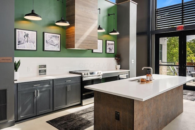 kitchen with stainless steel range with electric cooktop, a high ceiling, light countertops, a sink, and hanging light fixtures