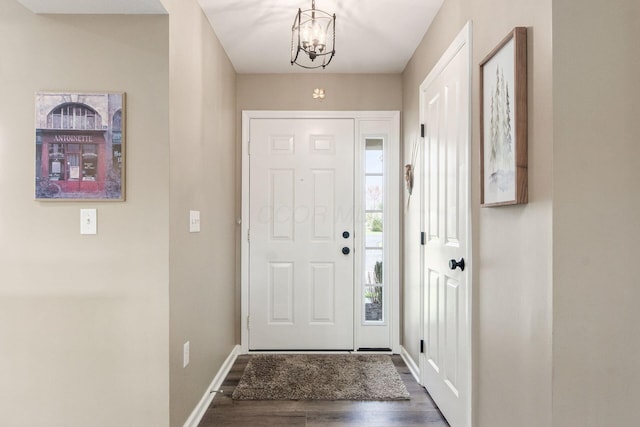 foyer entrance featuring dark wood finished floors, baseboards, and an inviting chandelier