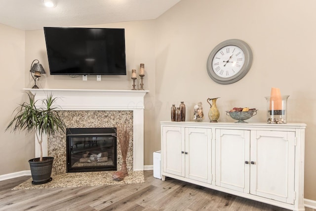 living room featuring a high end fireplace, baseboards, and light wood finished floors