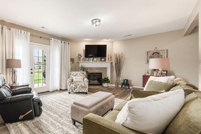 living room featuring a tiled fireplace, visible vents, and wood finished floors