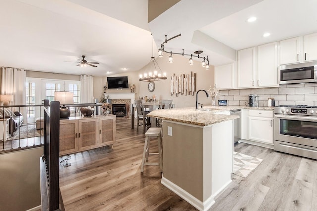 kitchen with a sink, a glass covered fireplace, ceiling fan, light wood finished floors, and appliances with stainless steel finishes